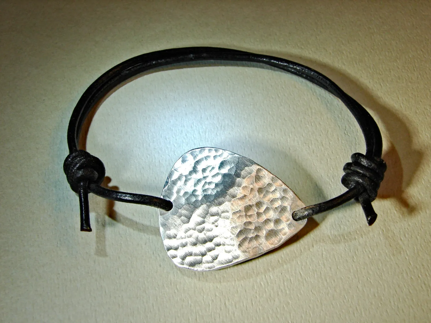 Hammered aluminum guitar pick on black leather cord