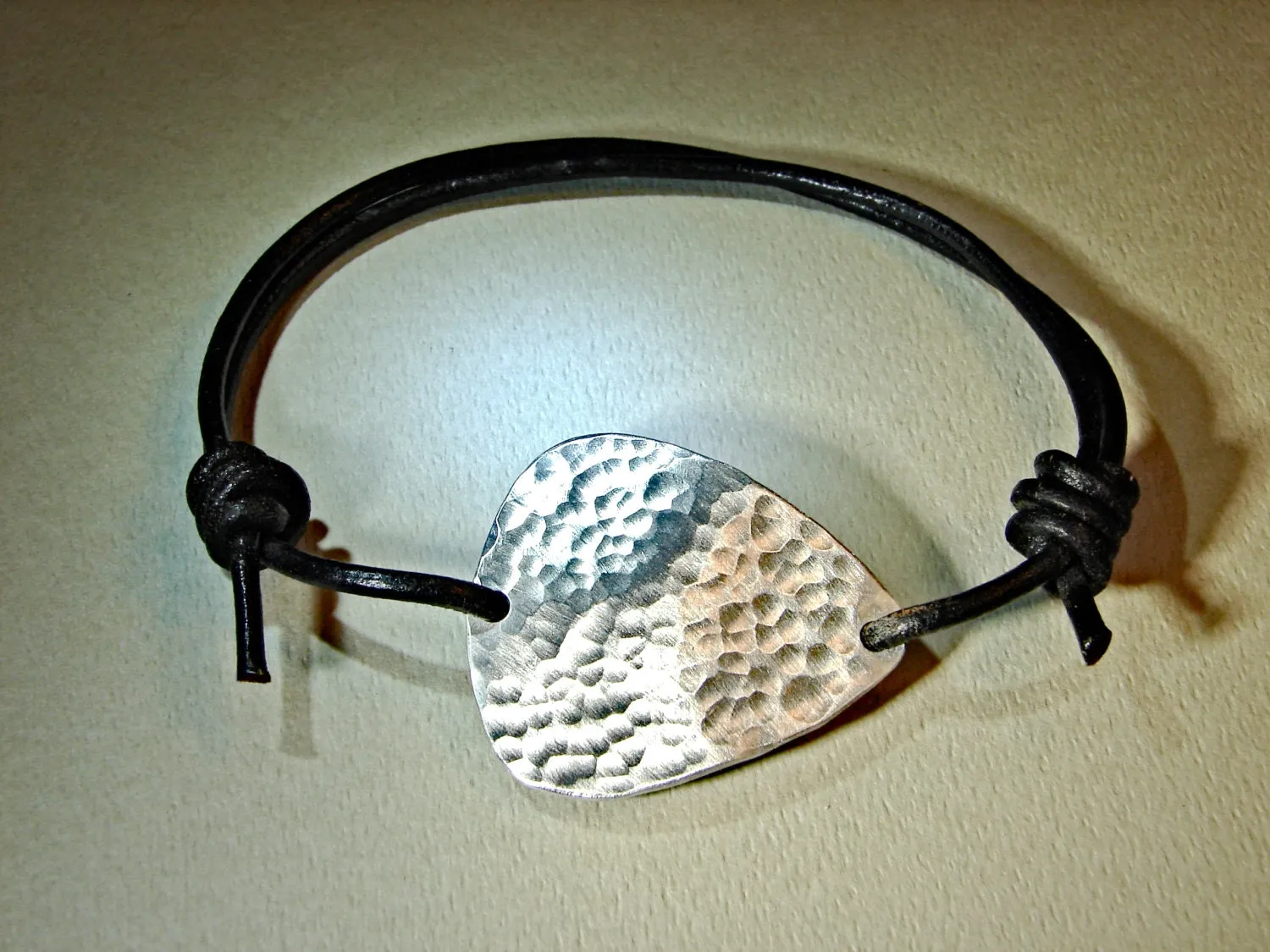 Hammered aluminum guitar pick on black leather cord