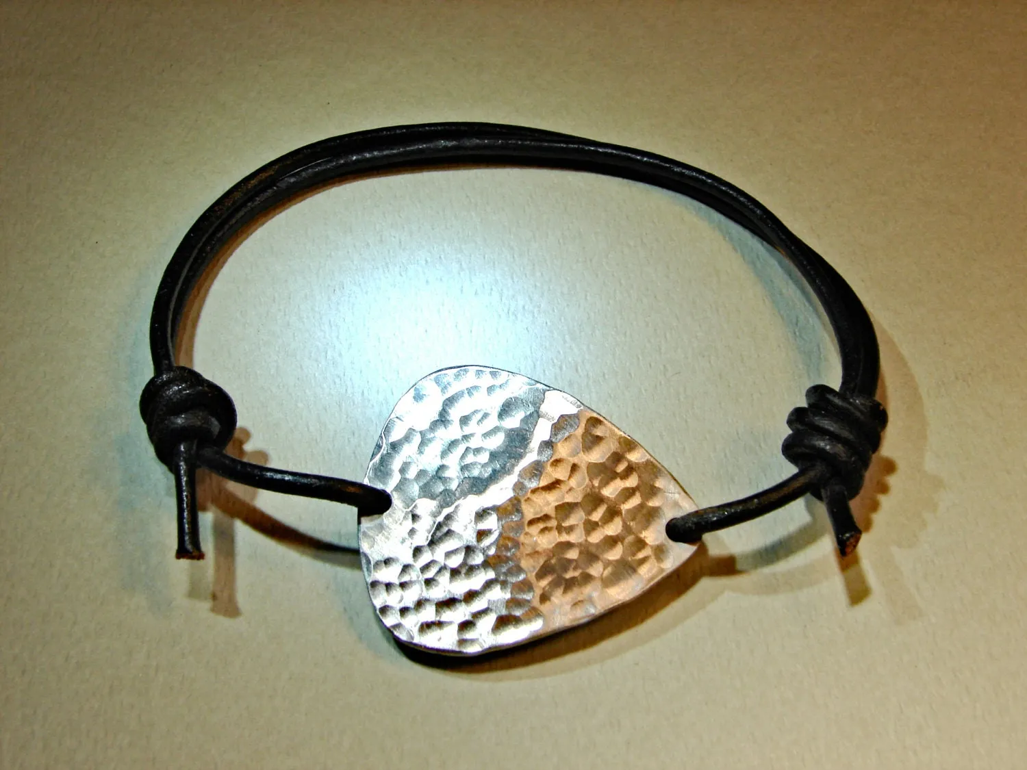 Hammered aluminum guitar pick on black leather cord
